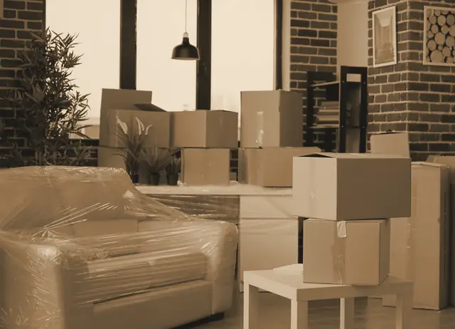 Salón con el sofá envuelto en film transparente y cajas de cartón apiladas antes de la mudanza